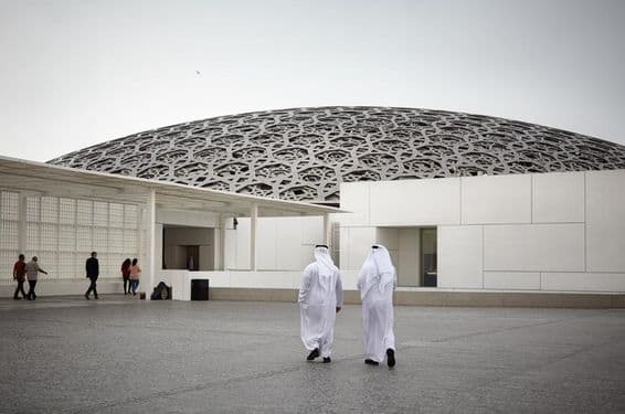 Touristes au musée du Louvre d'Abou Dhabi et deux personnes en vêtements traditionnels émiratis blancs.