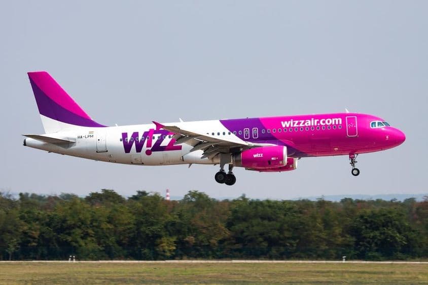 Avion Wizz Air volant à basse altitude avec une forêt en arrière-plan.
