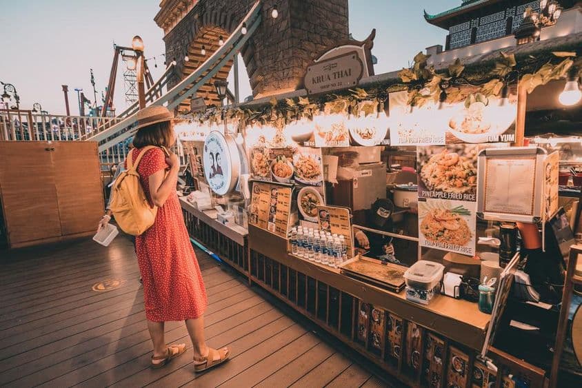Femme en robe rouge à pois regardant les cuisines nationales au Global Village de Dubaï.