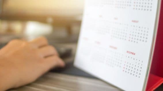 Une main à côté d'un calendrier, avec les mois flous, décembre clairement visible.