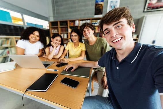 Des étudiants étudiant dans une bibliothèque, avec un ordinateur portable, un téléphone et un bloc-notes en papier sur le bureau.