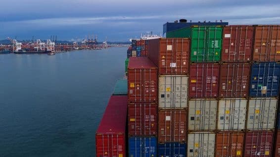 À gauche, une baie d'un port maritime est visible, à droite des conteneurs empilés.