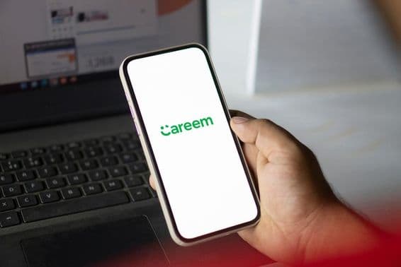 Une main tenant un téléphone avec l'application Careem, avec un carnet visible en arrière-plan.