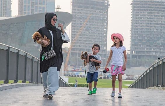 Une famille de quatre personnes devant les gratte-ciels de Dubaï, avec la mère et un enfant tenant un chien.