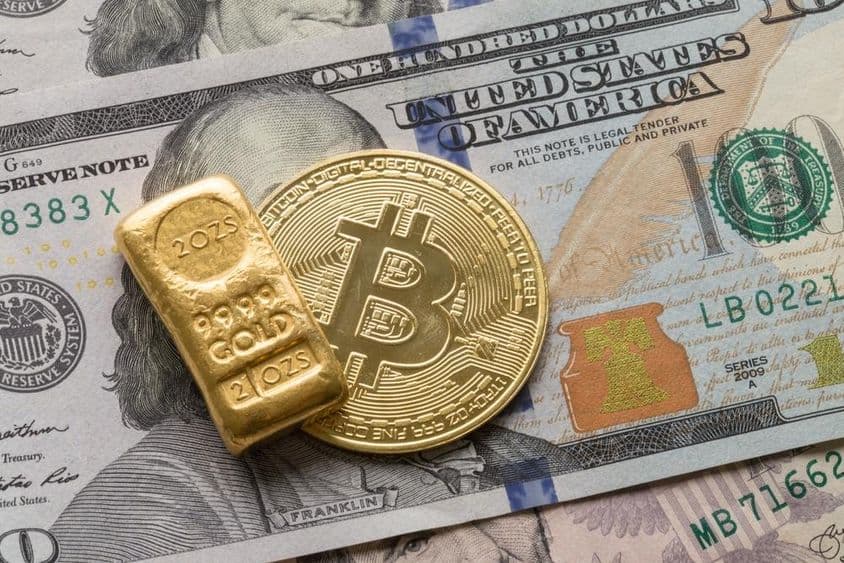 Un lingot d'or d'investissement et une pièce Bitcoin sur un billet de 100 dollars.