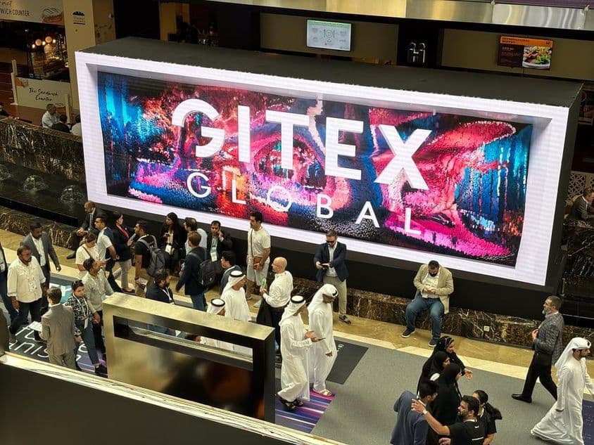 Gitex Global en arrière-plan avec des gens, principalement des hommes et des femmes émiratis au premier plan.