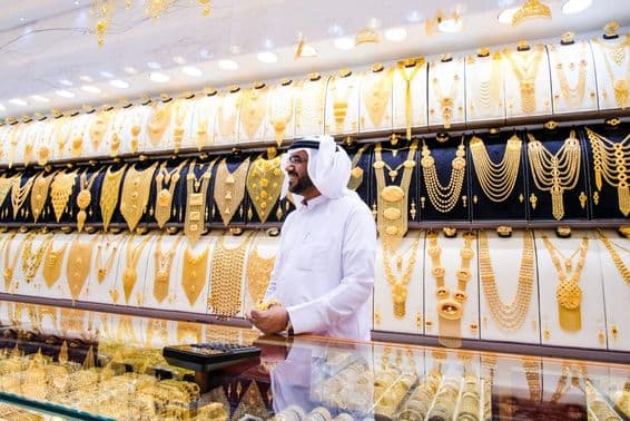 Vendeur d'or à Dubaï, avec un fond de nombreux colliers en or, le vendeur en tenue blanche traditionnelle.
