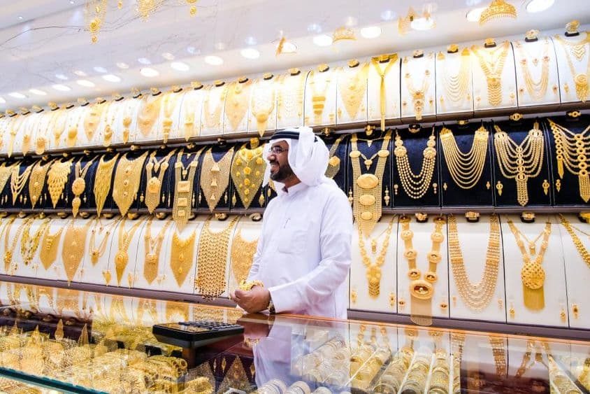Vendeur d'or à Dubaï, avec un fond de nombreux colliers en or, le vendeur en tenue blanche traditionnelle.