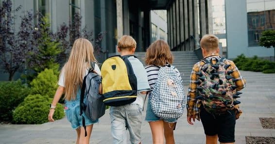 Étudiants portant des sacs à dos devant une entrée d'école.