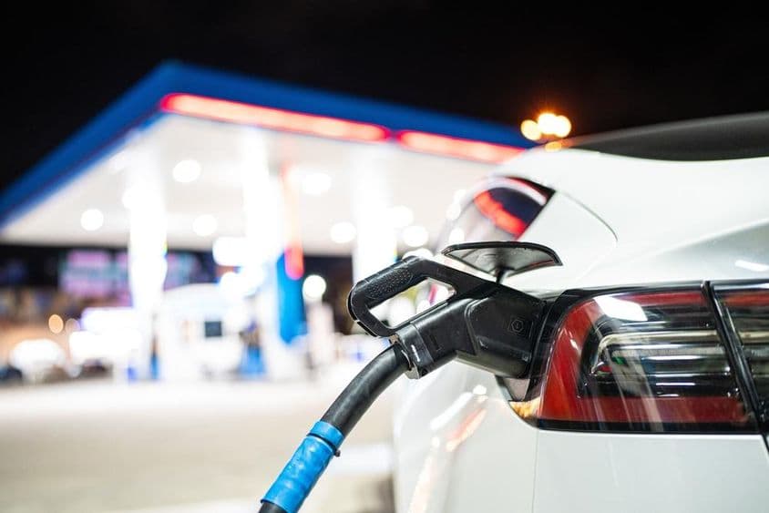 Une Tesla en charge, avec une station-service en arrière-plan.