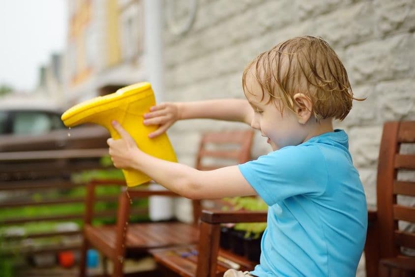 Un petit enfant versant de l'eau hors d'une botte tout en souriant.