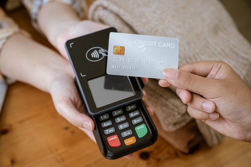 Une carte bancaire tenue dans une main, avec un lecteur de cartes en arrière-plan.