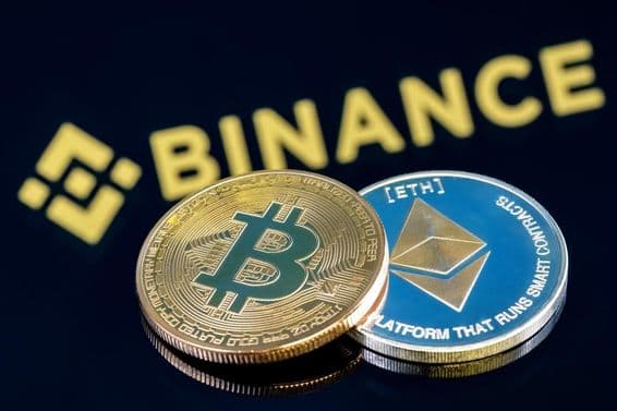 Inscription Binance à l'arrière-plan sur une table noire avec une pièce de Bitcoin et une pièce d'Ethereum.