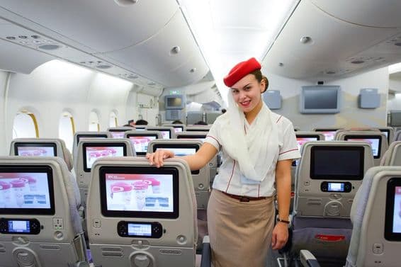 Intérieur d'un avion Emirates avec une hôtesse de l'air au premier plan.