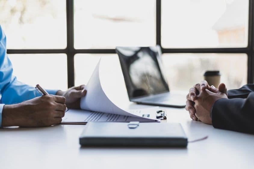 Deux individus assis l'un en face de l'autre pendant un entretien d'embauche, avec un cahier posé sur la table entre eux.