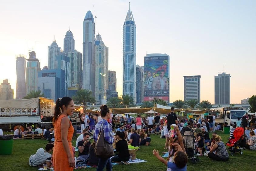 Des gens à Dubaï assis dans un parc, gratte-ciels en arrière-plan.
