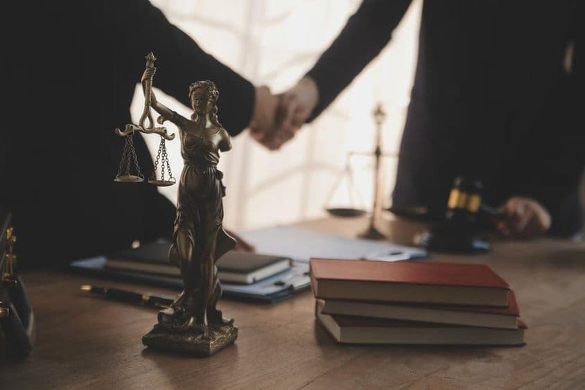 Un avocat est photographié en train de négocier avec un client, avec une statue de Justitia visible sur la table.