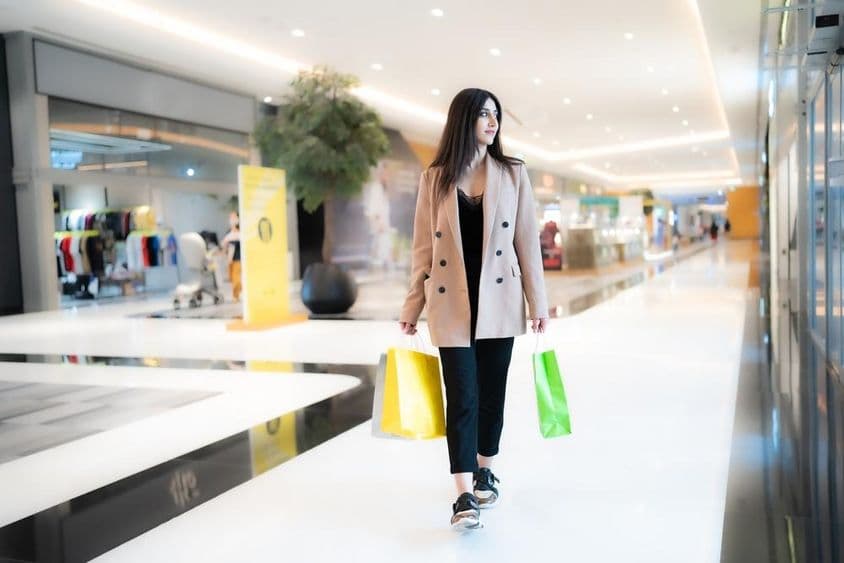 Une femme faisant du shopping au Dubai Mall, tenant deux sacs, avec des boutiques en arrière-plan.
