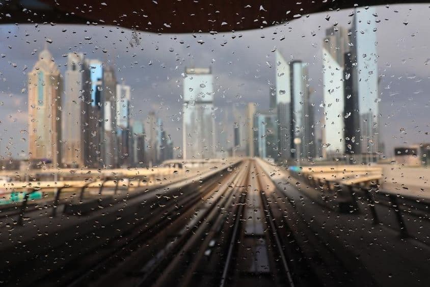 Pluie vue à travers une fenêtre de métro à Dubai avec des gratte-ciels en arrière-plan.