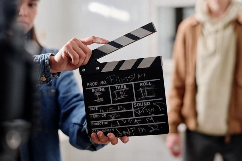 Clap de cinéma avec écriture à la craie, deux personnes à côté.