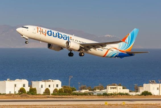 avion de flydubai volant à basse altitude, avec de petites maisons blanches et la mer en arrière-plan.