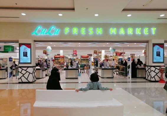 Entrée d'un magasin LuLu dans un centre commercial, avec deux personnes assises, une femme et un enfant, vues de dos.