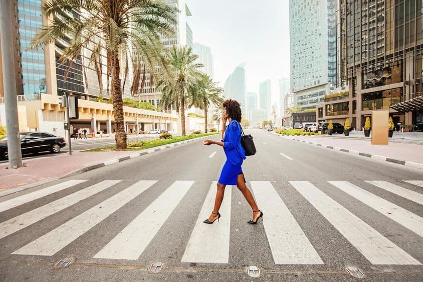 À Dubaï, une femme traverse un passage piéton sur une route vide, avec des maisons visibles en arrière-plan.