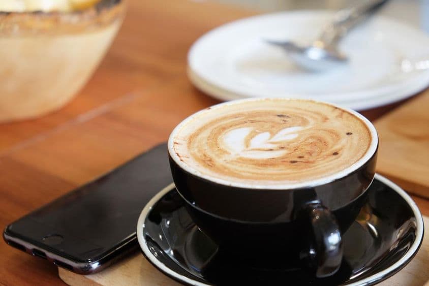 Une tasse de cappuccino sur une table avec un téléphone à côté.
