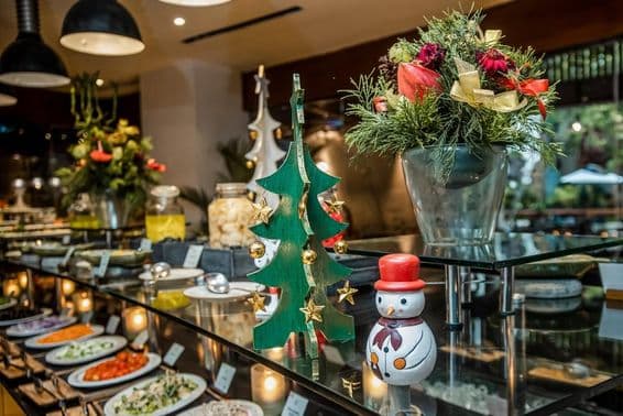 Petit bonhomme de neige dans un restaurant sur un comptoir de légumes, à côté d'un sapin de Noël en bois.