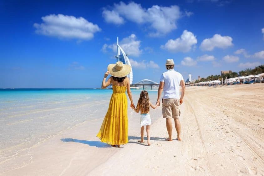 Jeune famille avec une fille marchant sur la plage, Burj Al Arab en arrière-plan.