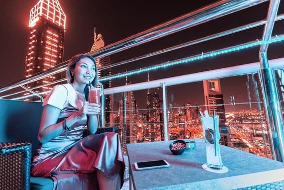 Jeune femme sirotant un cocktail sur la terrasse d'un bar rooftop à Dubai.