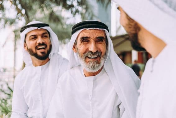 Un homme âgé émirati conversant avec deux jeunes individus.