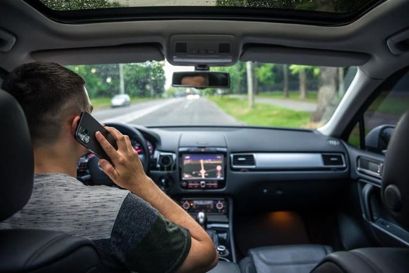 Jeune homme utilisant son téléphone en conduisant une voiture.
