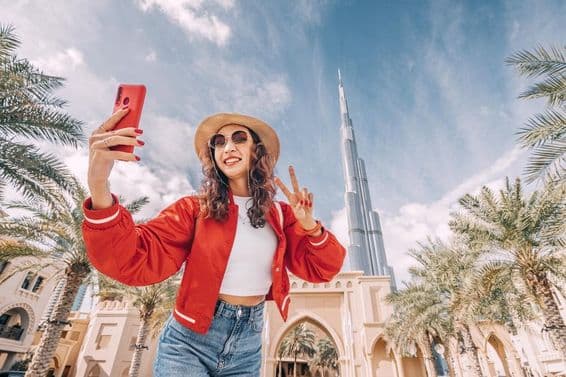 Jeune femme, en haut rouge, prenant un selfie avec le Burj Khalifa en arrière-plan.
