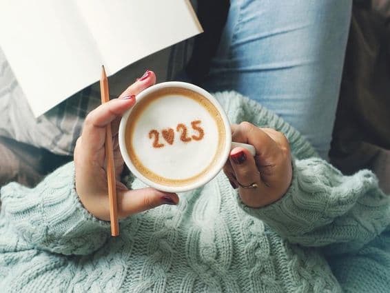 Une tasse de café tenue par une femme, avec 2025 écrit à l'intérieur.
