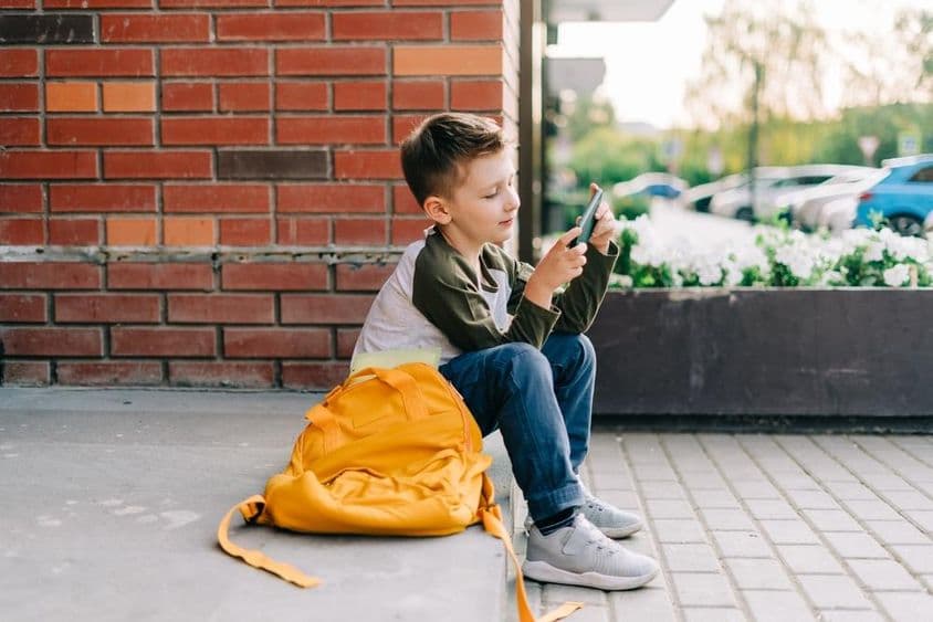 Garçon utilisant un téléphone sur les marches de l'école.