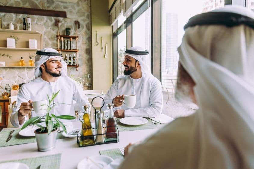 Trois hommes d'affaires buvant du thé à Dubaï, vêtus de tenues traditionnelles émiraties.