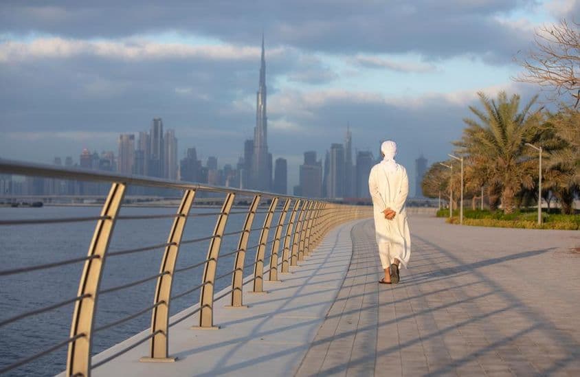 Emirati marchant sur un trottoir avec Burj Khalifa en arrière-plan.