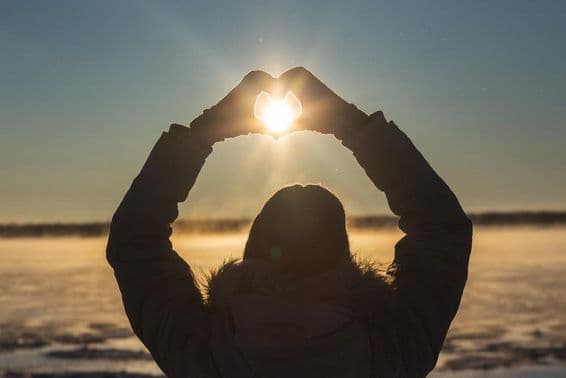 Femme formant des cœurs avec ses mains en extérieur lors d'un coucher de soleil givré.