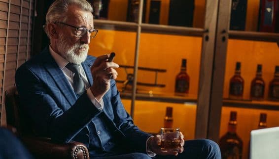 Homme retraité âgé utilisant un ordinateur portable, fumant, tenant un alcool cher.