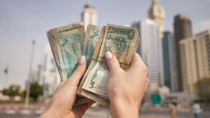 Une fille tenant la monnaie des Émirats arabes unis avec les gratte-ciel de Dubaï en arrière-plan.