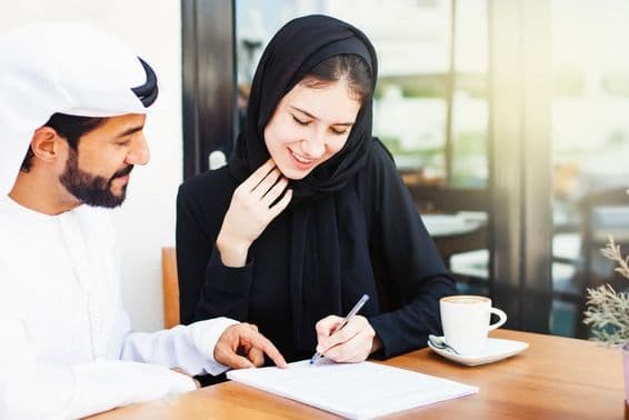 Homme arabe remettant des documents pour signature à une femme portant un hijab.