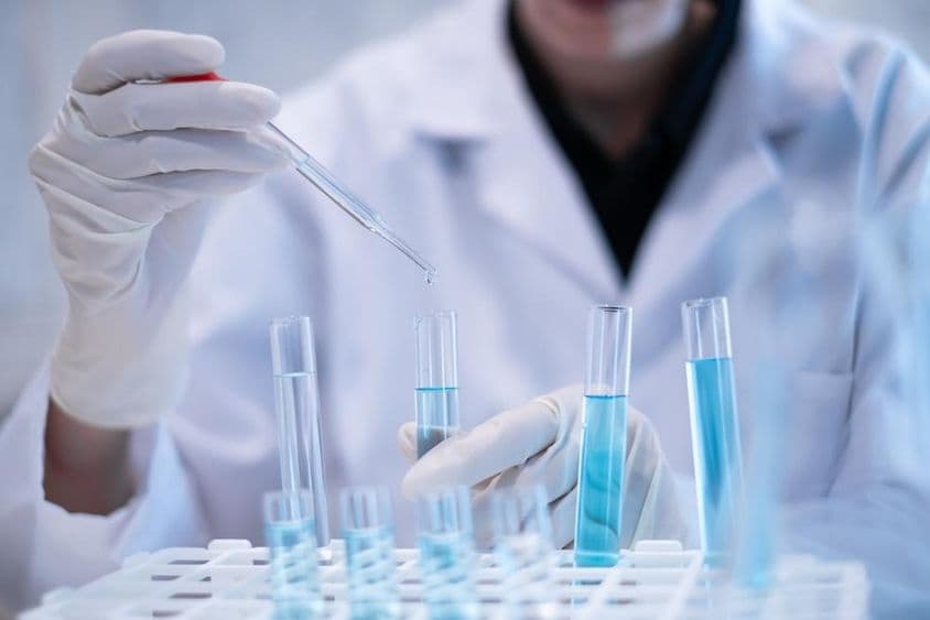 Scientifique pipetant un liquide bleu dans un tube à essai dans un laboratoire.