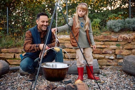 Petite fille aide son père à cuisiner sur un feu de camp en pleine nature pendant l'automne.