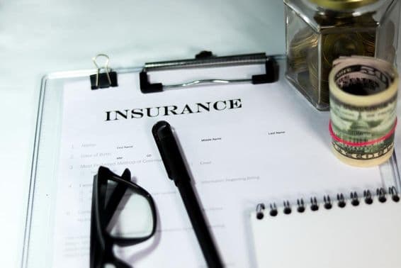 Formulaire d'assurance avec boîte à pièces, paquet de dollars, stylo et lunettes.