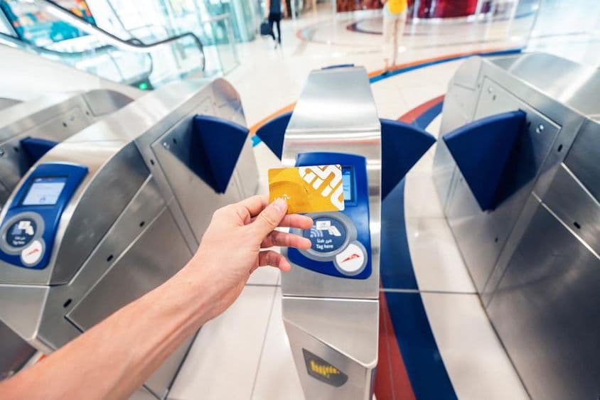 Un passager masculin utilise une carte NOL dorée au métro de Dubaï pour franchir un tourniquet et voyager dans le premier wagon.
