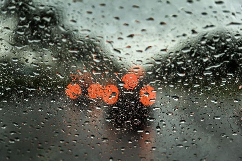 Journée pluvieuse à Dubaï avec des lumières de voiture visibles au loin, vue à travers une fenêtre de voiture avec des gouttes de pluie.