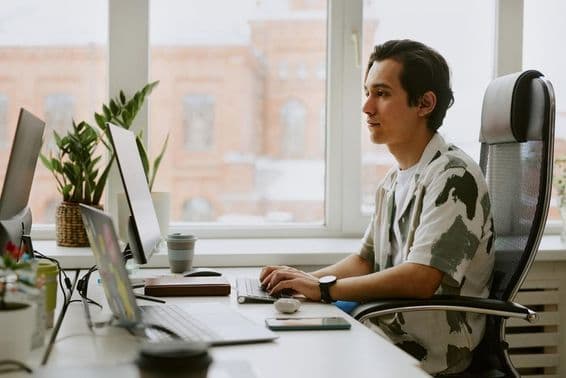 Jeune programmeur assis à un bureau, codant sur un ordinateur dans un bureau lumineux.