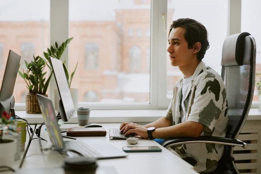 Jeune programmeur assis à un bureau, codant sur un ordinateur dans un bureau lumineux.