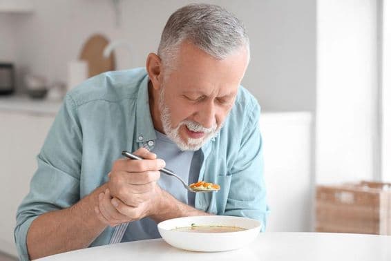 Homme âgé atteint de Parkinson mangeant à une table de cuisine.